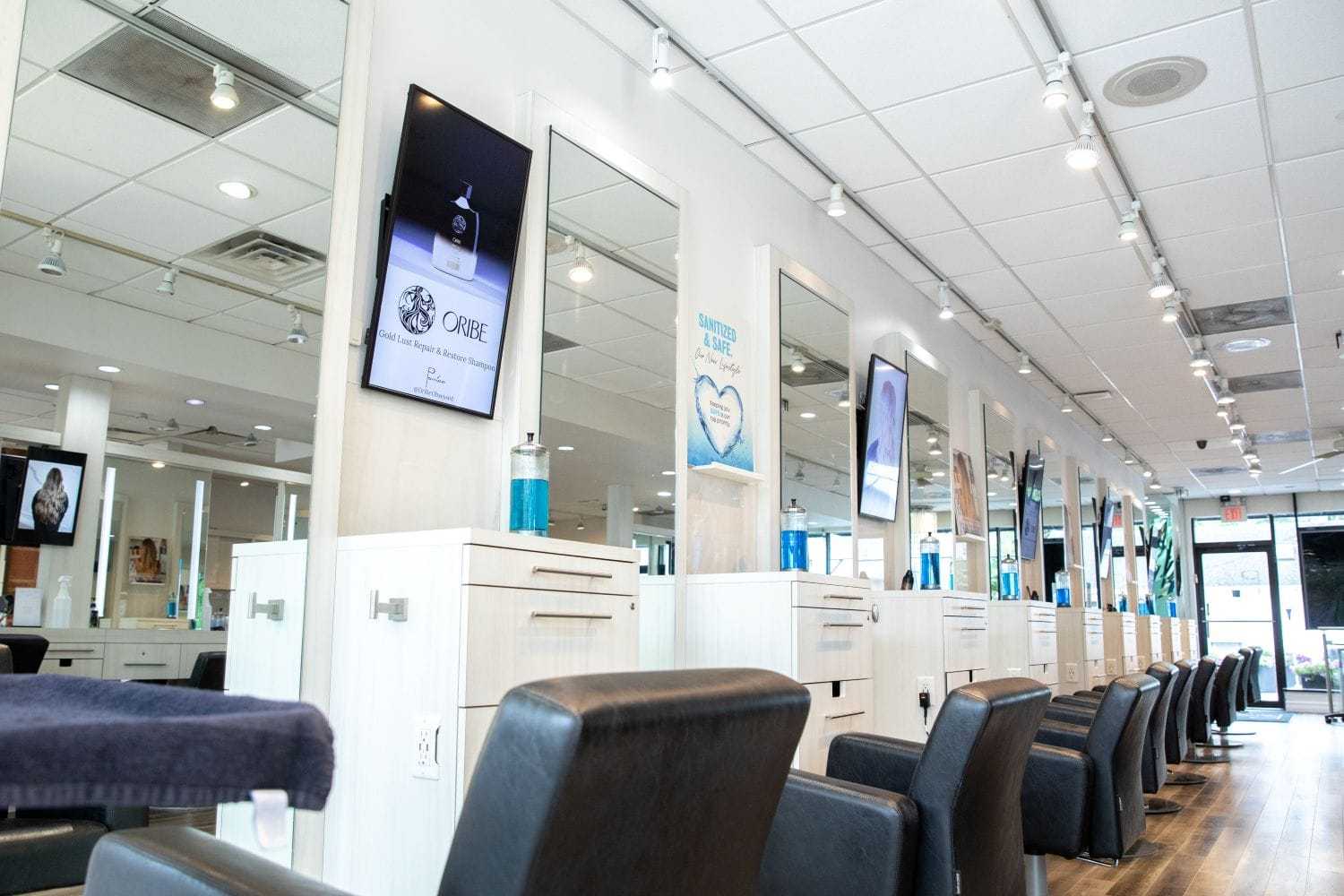 Modern salon interior with sleek chairs, mirrors, and digital screens on white walls.