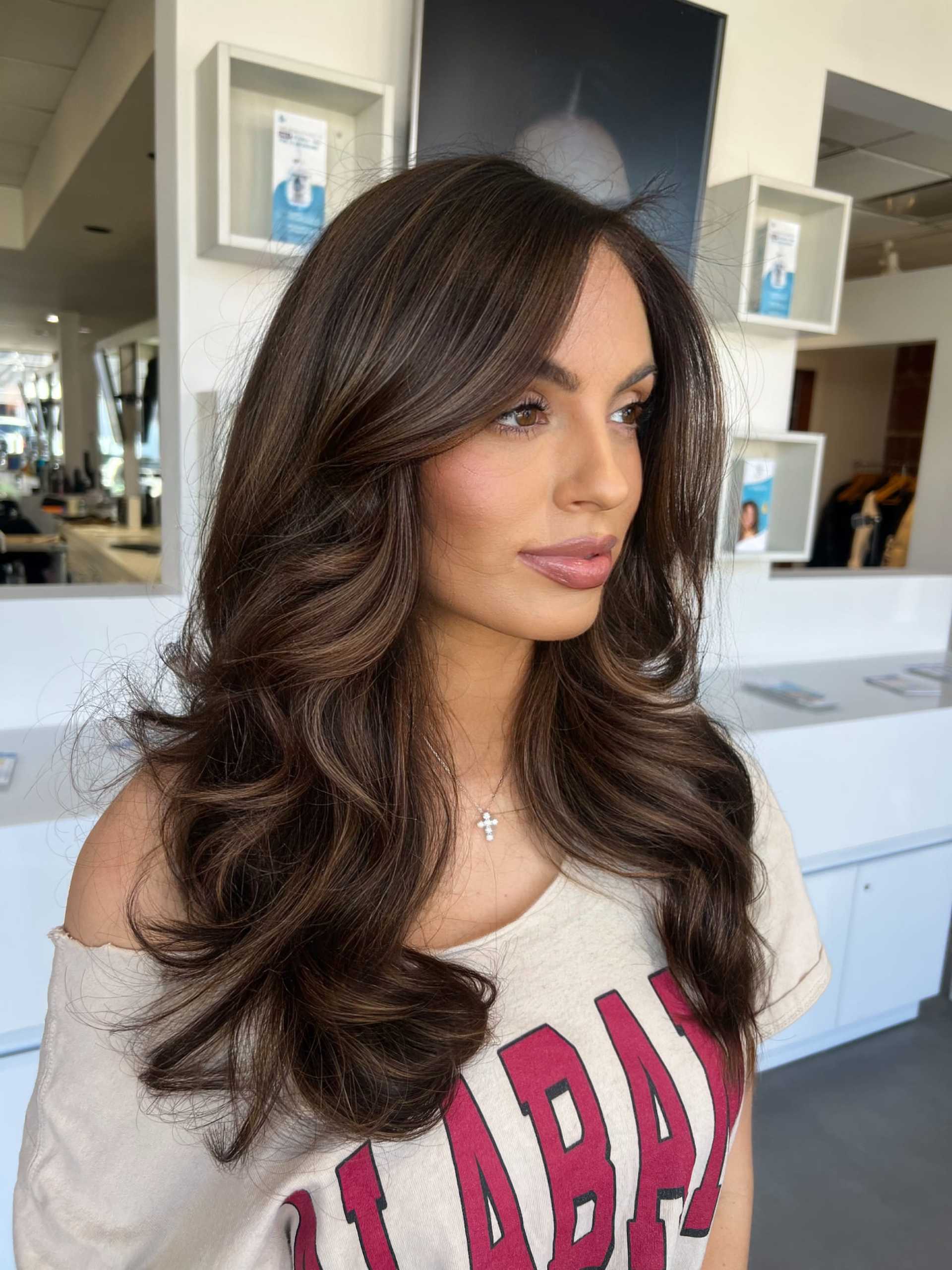 Woman with long wavy hair in a salon wearing an "Alabama" t-shirt.