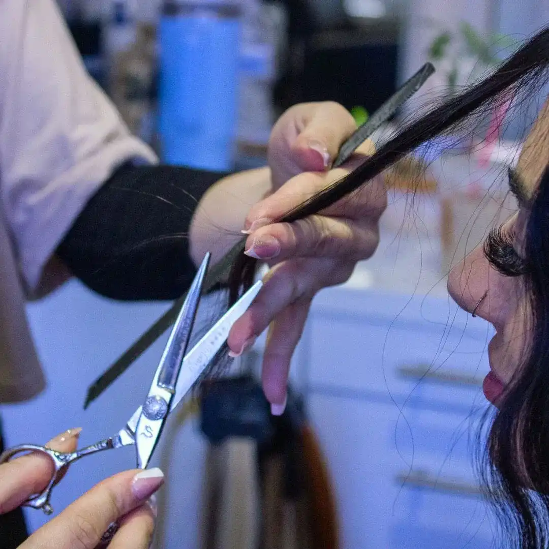 Hands trimming woman's hair with scissors in a salon.