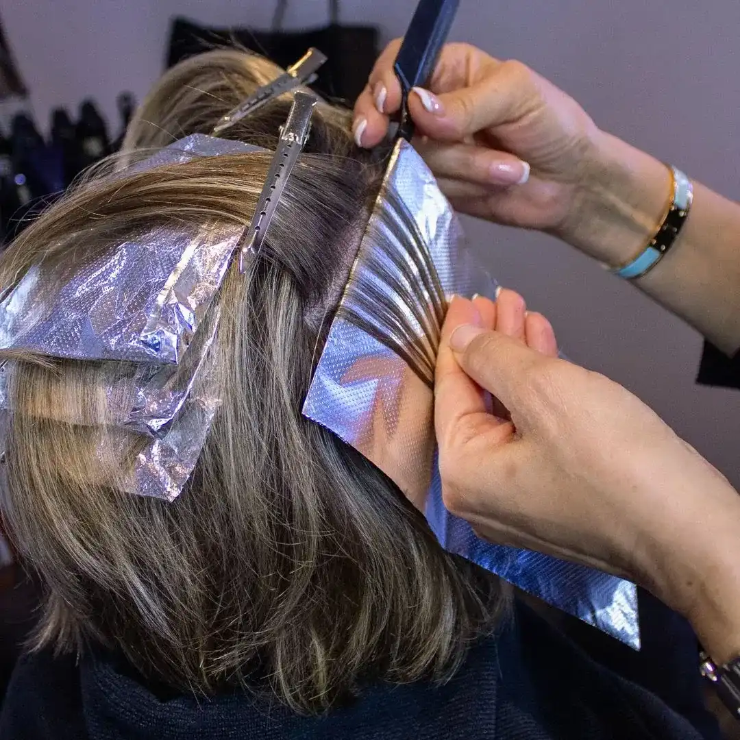 Hairdresser applying highlights to a client's hair using foils in a salon.