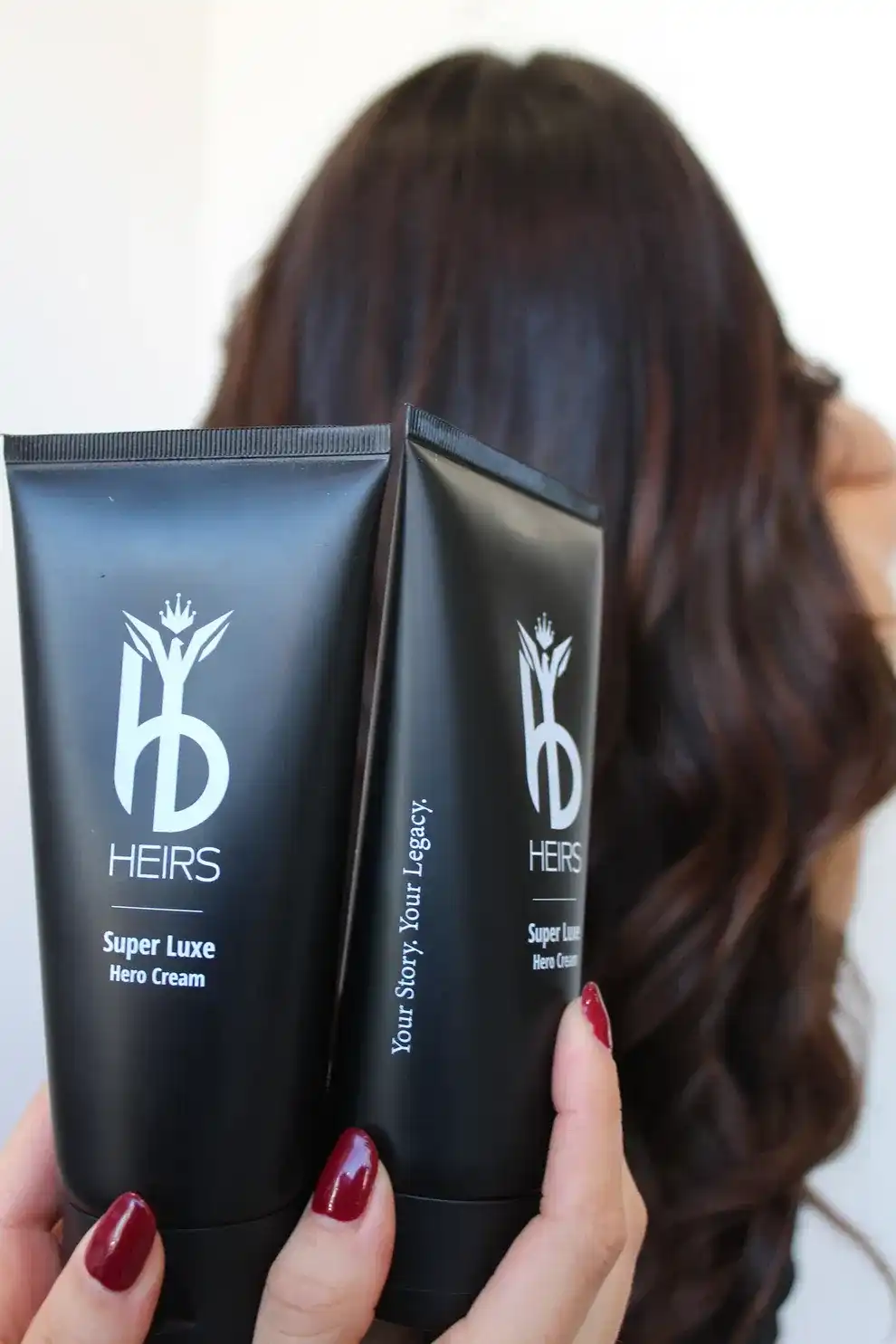 Heirs Super Luxe Hero Cream held with long, wavy hair in the background.